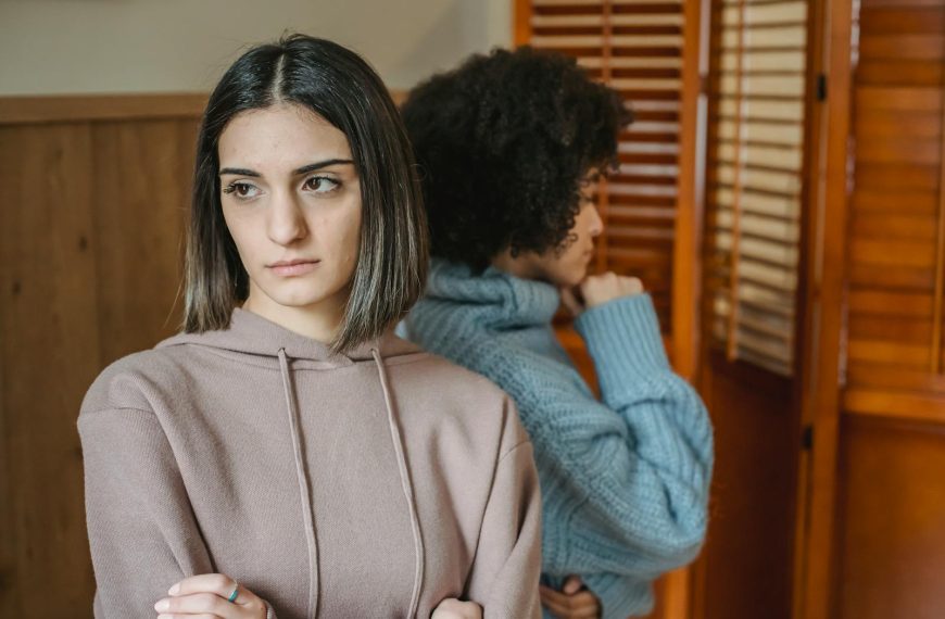 Upset multiracial women in casual wear standing in light room near wall with wooden folding screen while having conflict at home