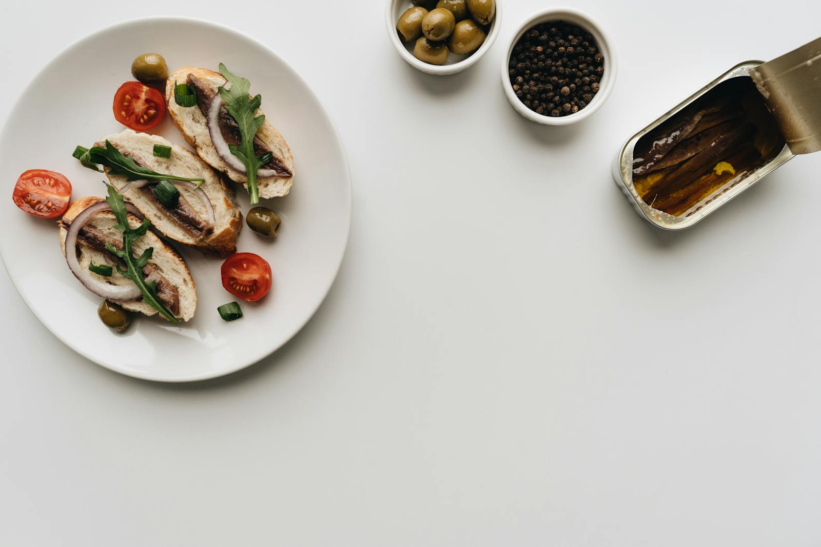 Top view of delicious Mediterranean dish with anchovies, olives, and tomatoes on white background.