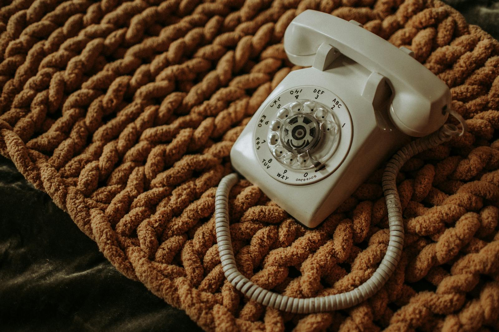 A classic white rotary phone resting on a textured brown mat, showcasing retro charm.