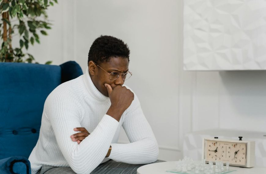 Thoughtful man in white sweater playing chess indoors, emphasizing strategy and focus.
