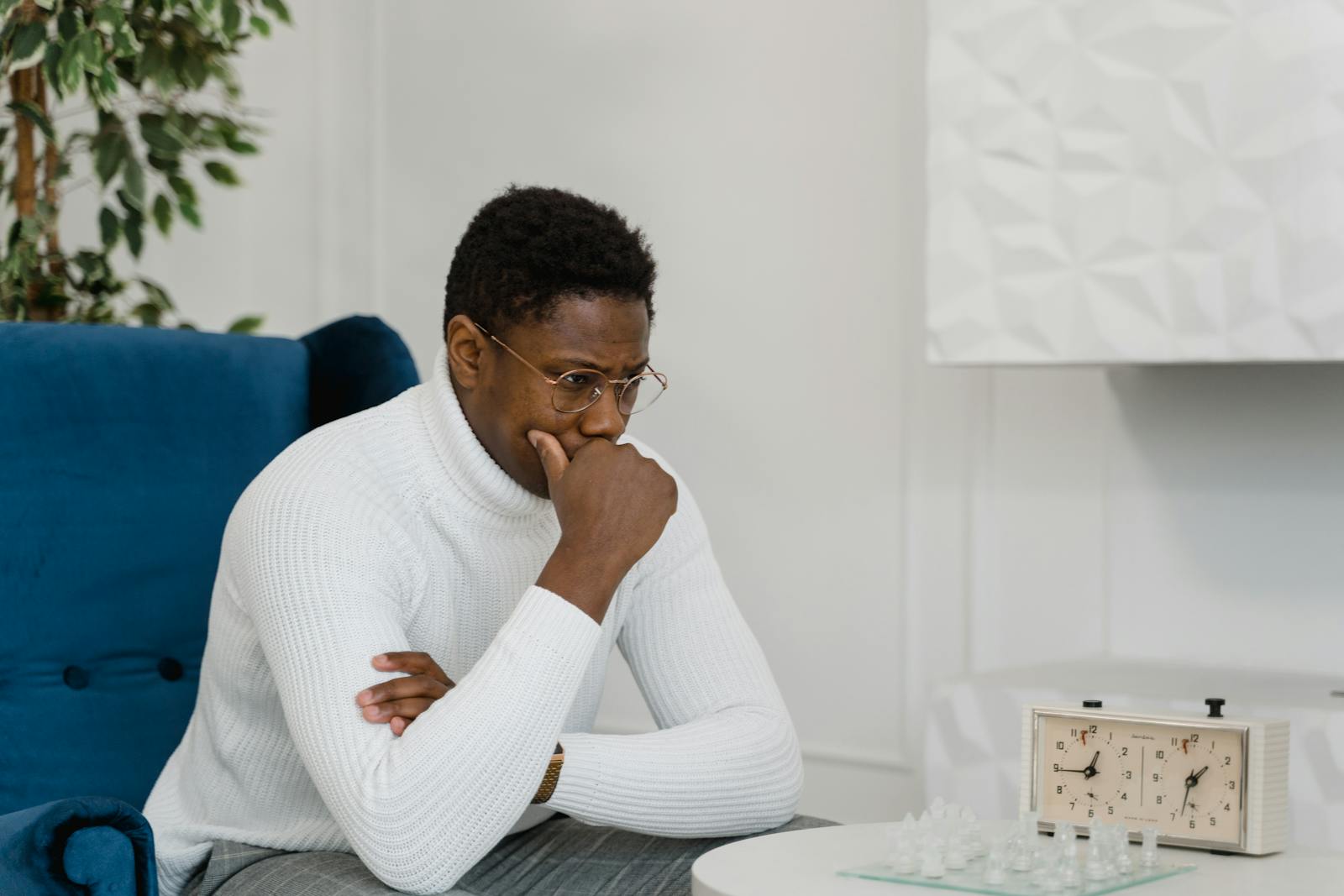 Thoughtful man in white sweater playing chess indoors, emphasizing strategy and focus.