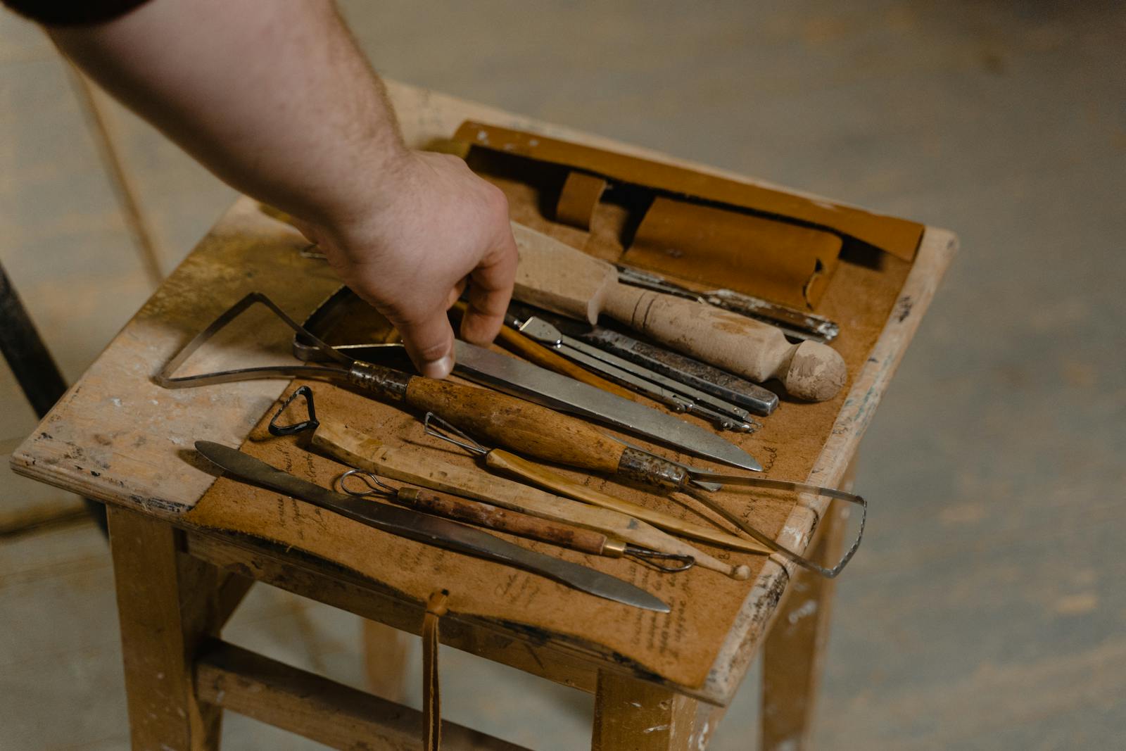 A close-up of artisan hand selecting tools on a wooden stool for woodwork.