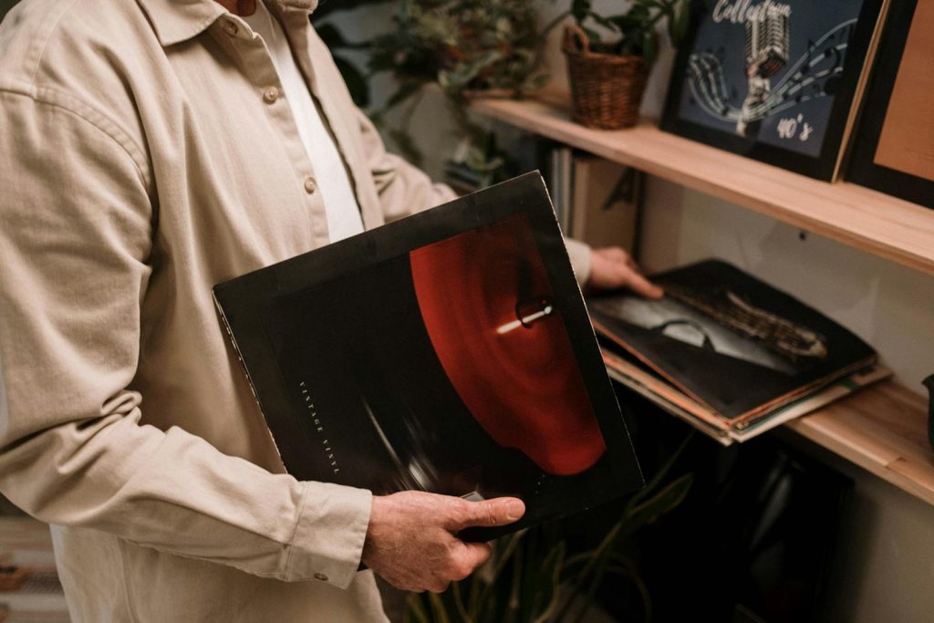 Adult holding vintage vinyl record, browsing a collection on a shelf indoors.