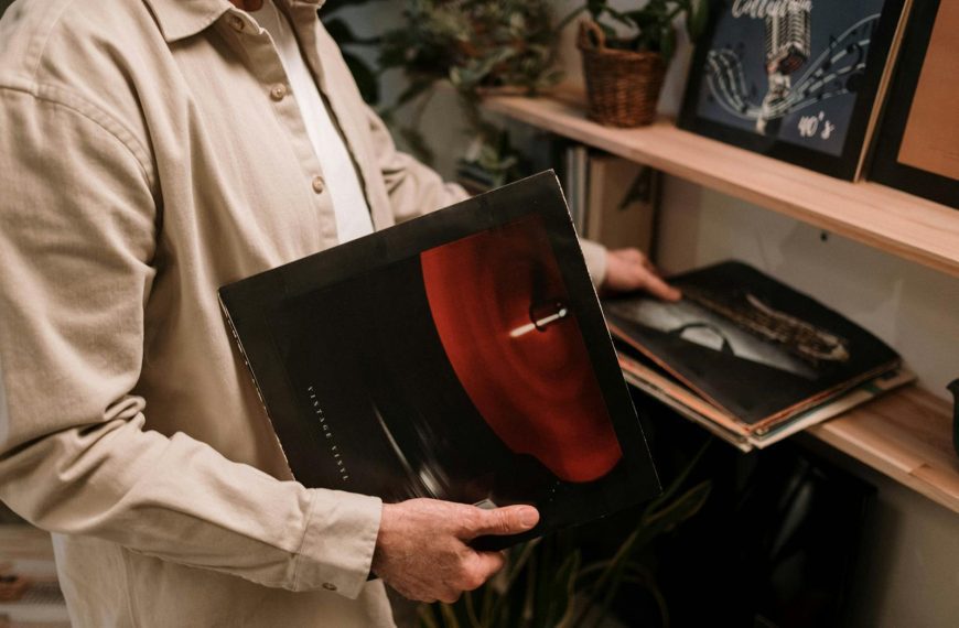 Adult holding vintage vinyl record, browsing a collection on a shelf indoors.