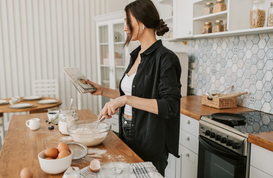 Woman in kitchen holding a cookbook and mixing ingredients for a recipe.