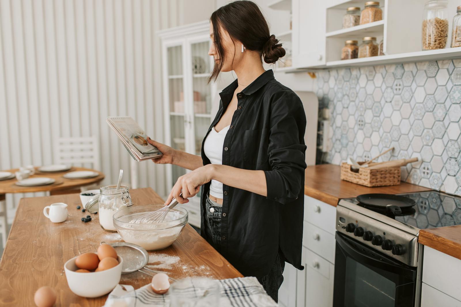 Woman in kitchen holding a cookbook and mixing ingredients for a recipe.