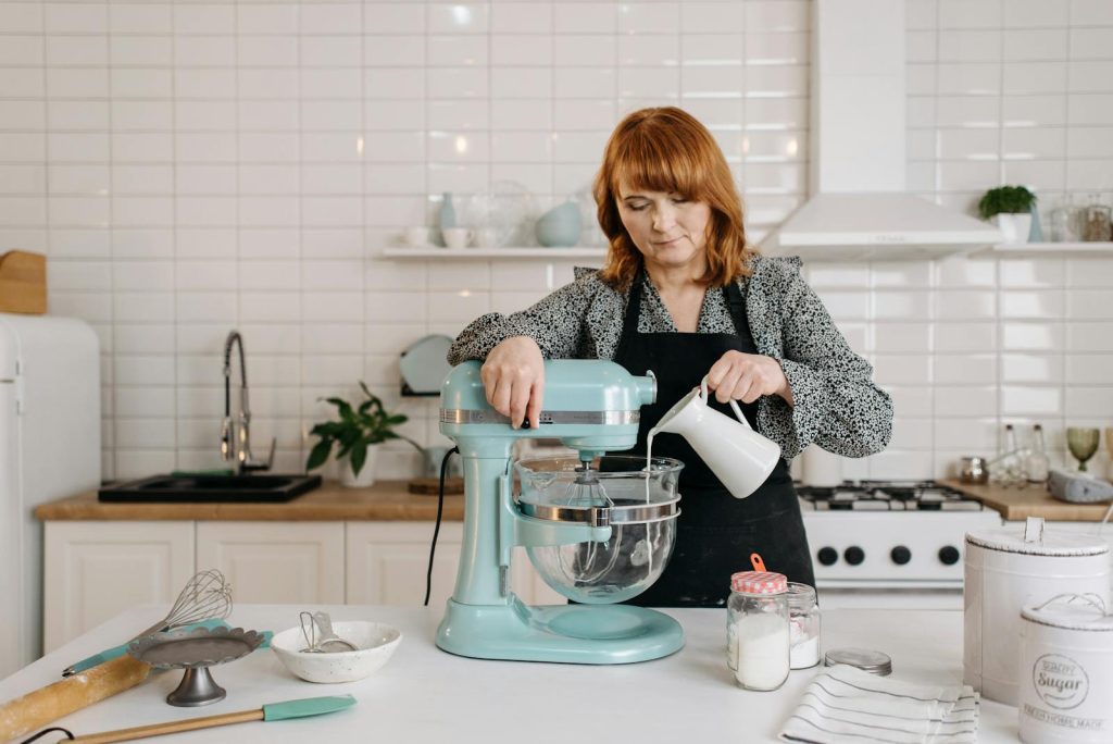 A woman pours milk into a stand mixer in a modern kitchen, preparing dough.