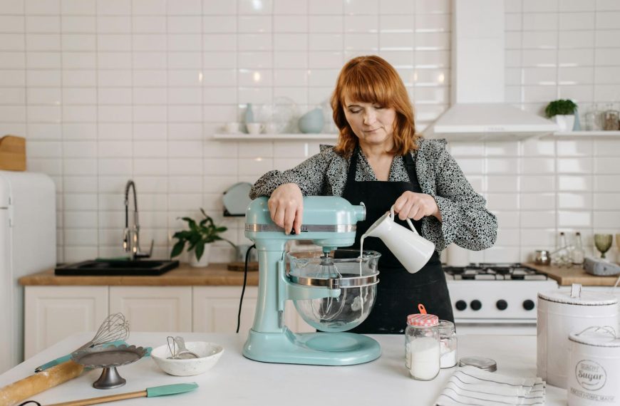 A woman pours milk into a stand mixer in a modern kitchen, preparing dough.