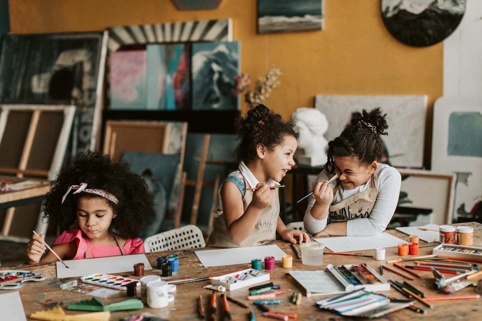 Three young girls enjoying a creative painting session with art supplies in a vibrant studio.