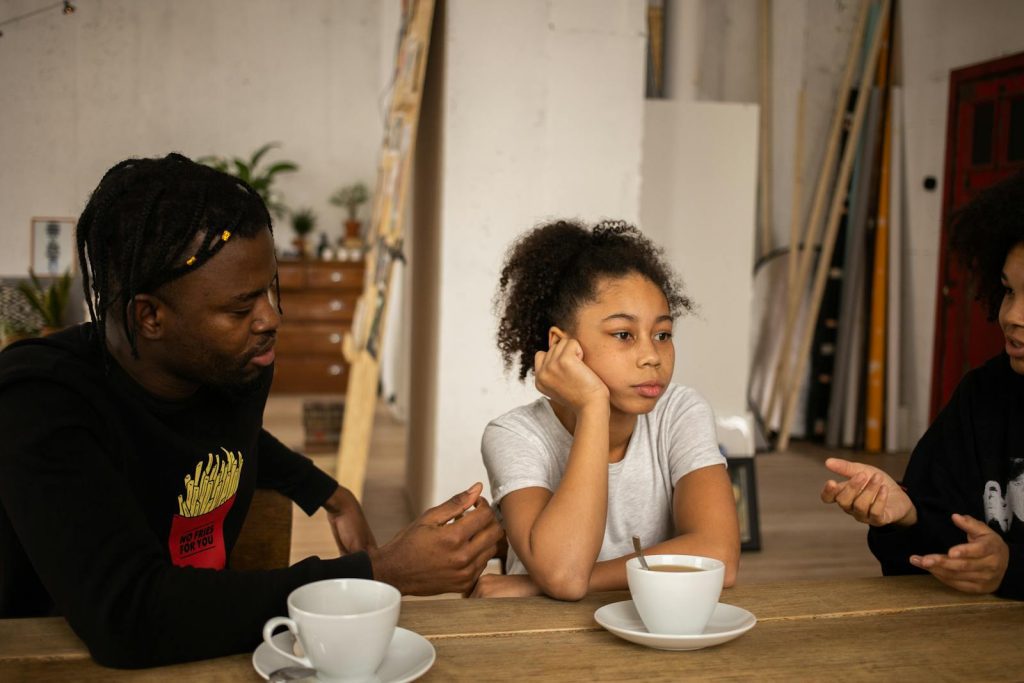 A family engages in a thoughtful discussion around a table with coffee indoors.
