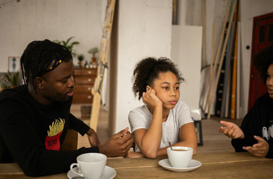 A family engages in a thoughtful discussion around a table with coffee indoors.