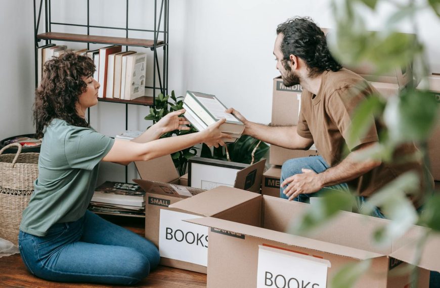 A couple organizing and packing books in cardboard boxes indoors, preparing for a move.