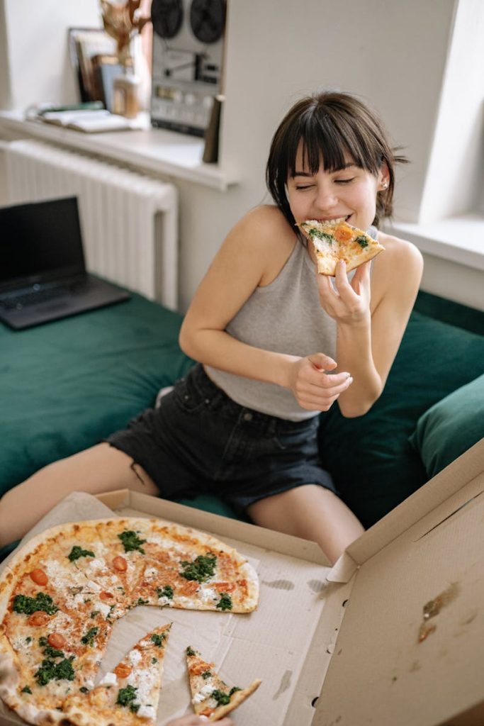 Woman in casual wear sitting on couch with pizza, looking happy and relaxed.