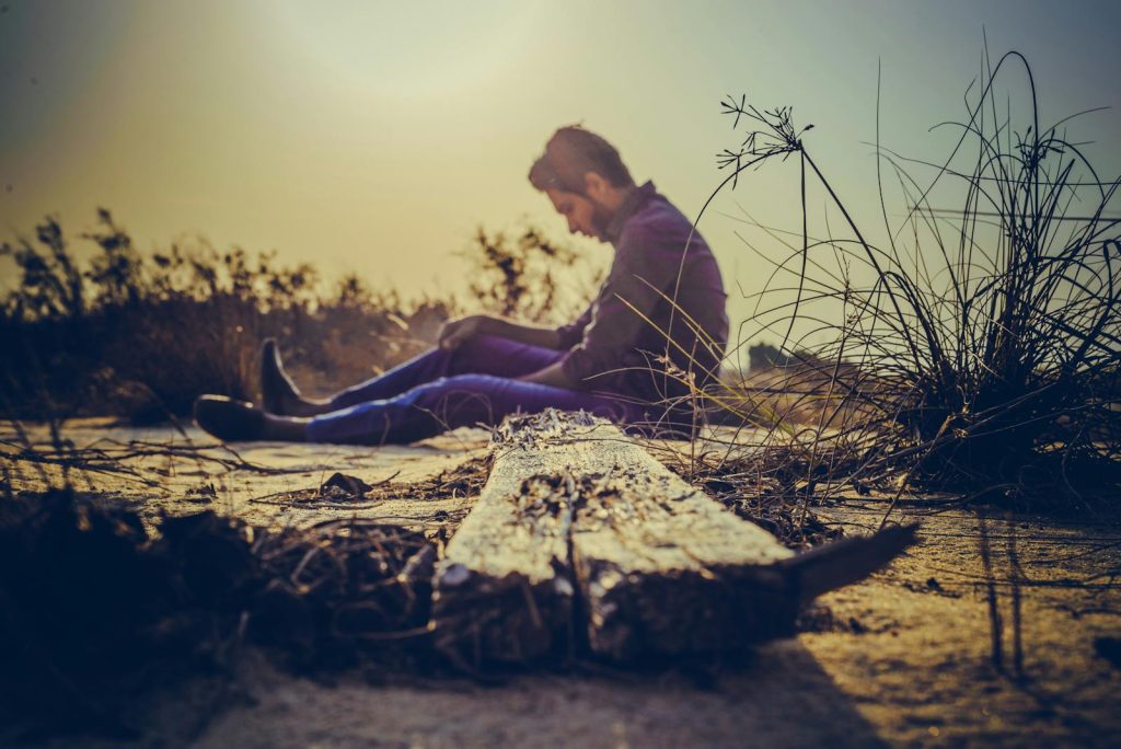 A man sits alone on sandy terrain at sunset, capturing solitude in nature's calm.