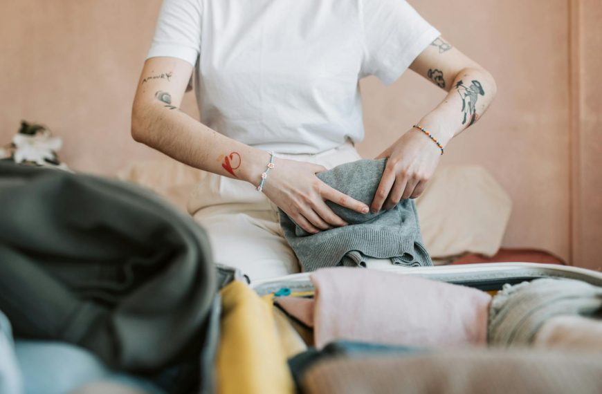 Woman with tattoos packing clothes into a suitcase for travel.