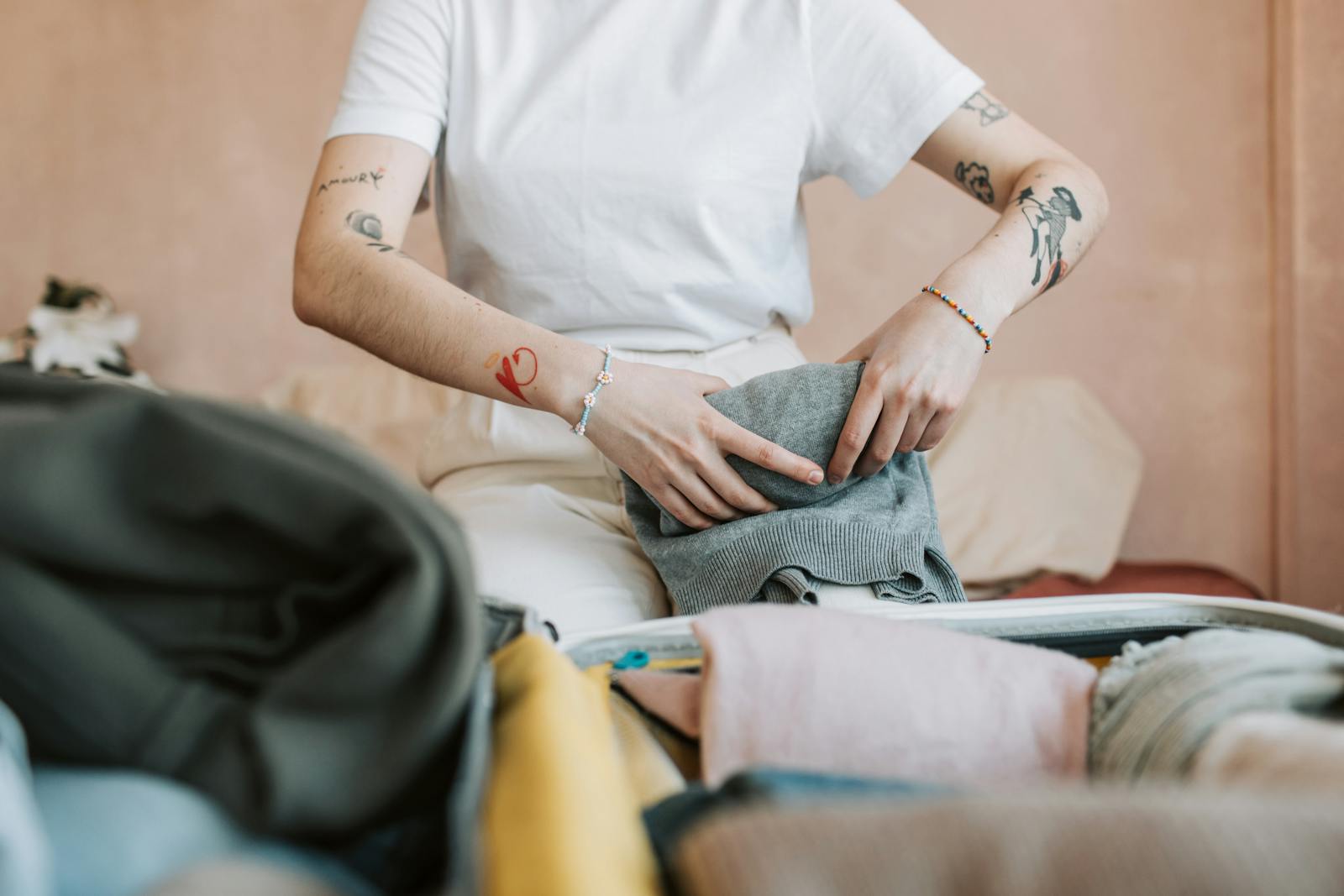 Woman with tattoos packing clothes into a suitcase for travel.