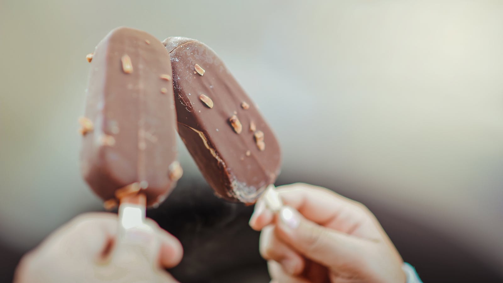Close-up of two chocolate ice cream bars with nuts held by hands.