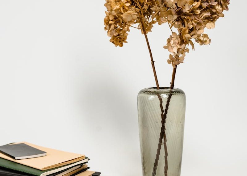 A minimalist arrangement featuring dried hydrangeas in a vase next to books and a magnifying glass.