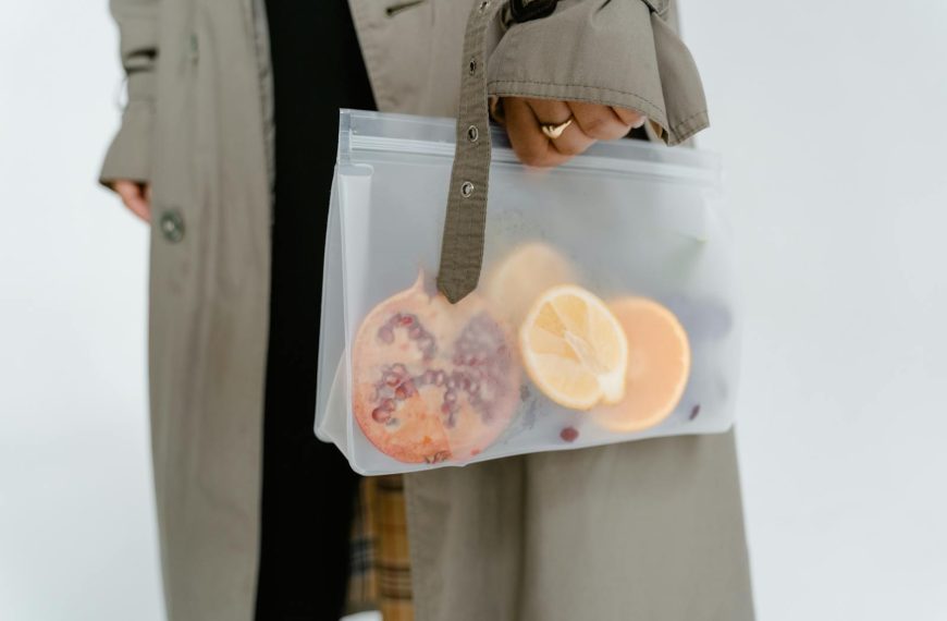 A person holds a zip lock bag containing sliced and whole fruits including a pomegranate.