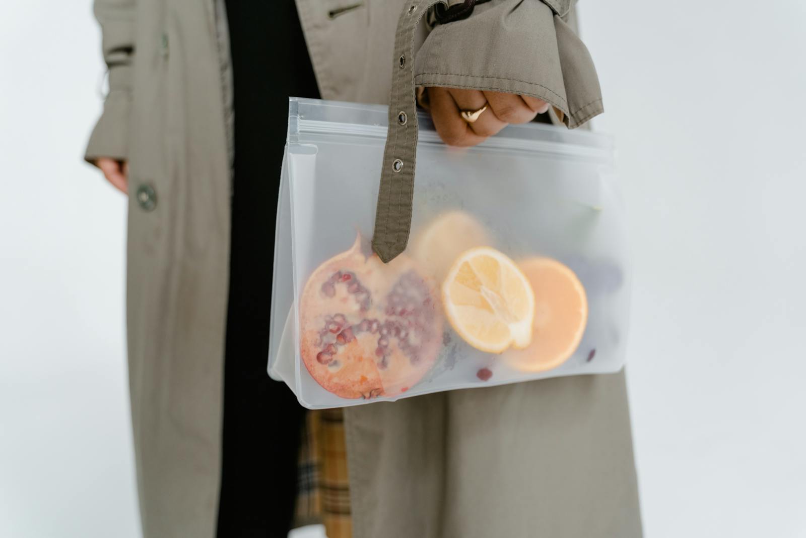 A person holds a zip lock bag containing sliced and whole fruits including a pomegranate.