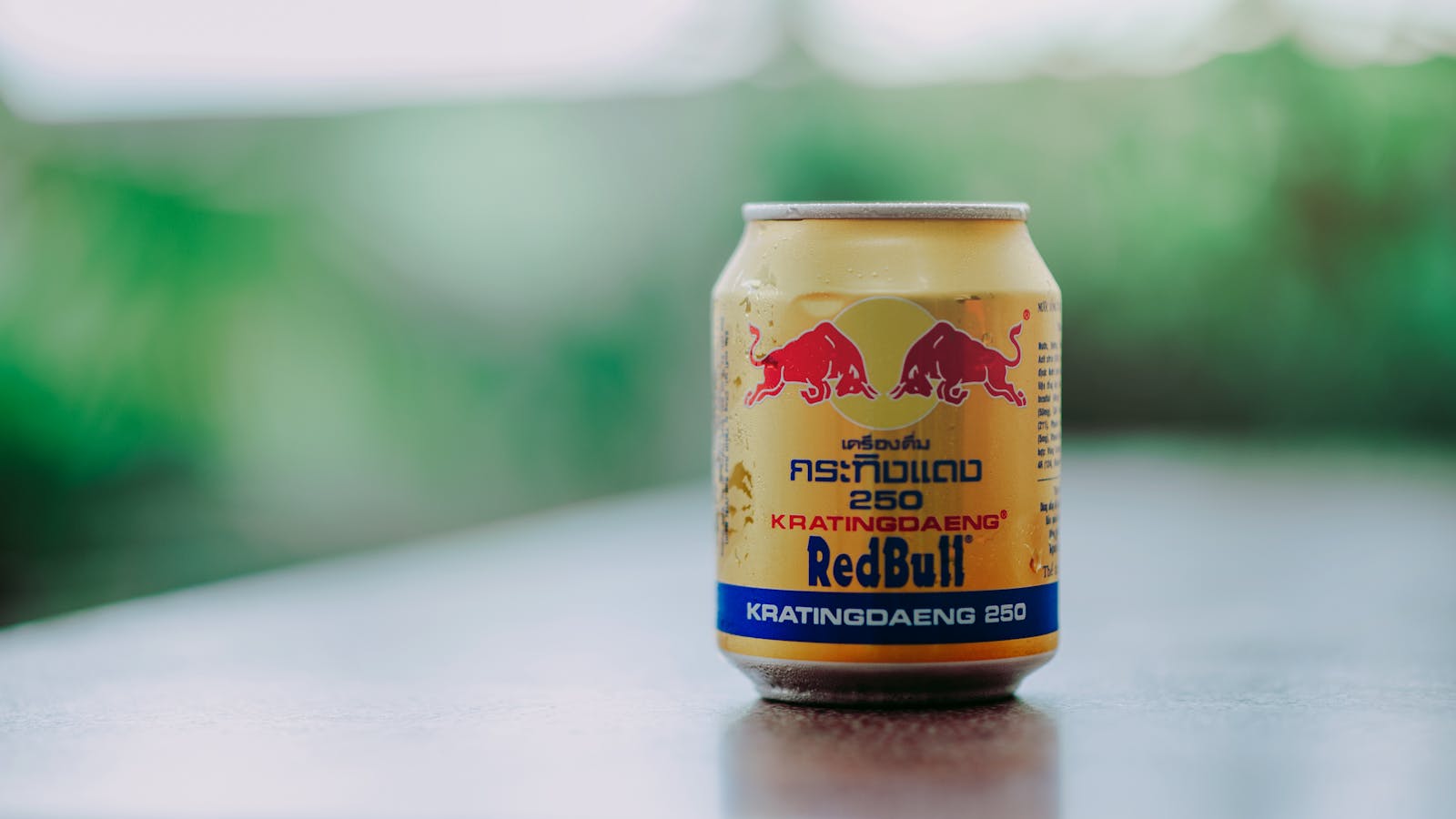 Close-up image of a Kratingdaeng energy drink can with condensation outdoors, featuring vibrant colors.