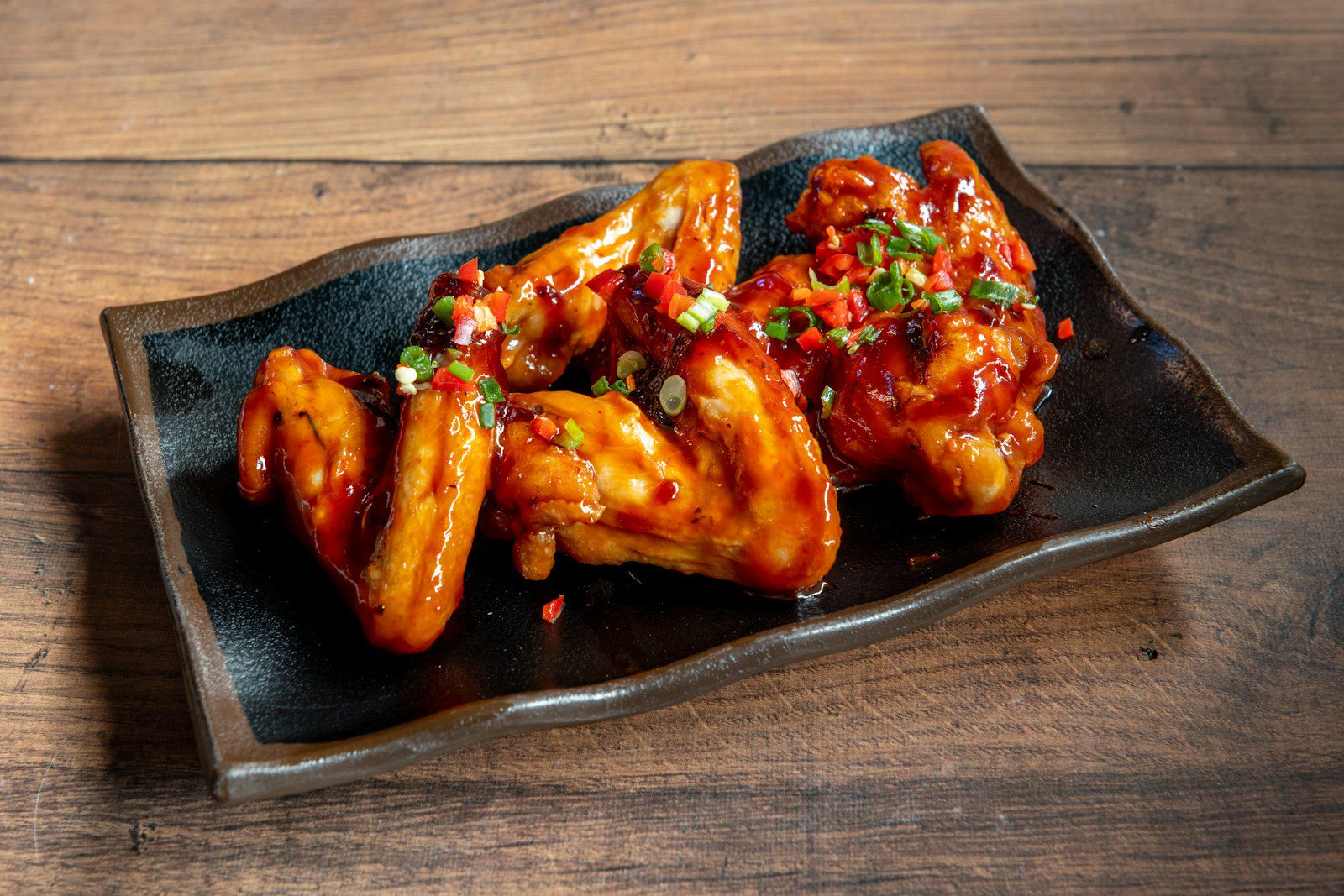 A black plate topped with wings covered in sauce