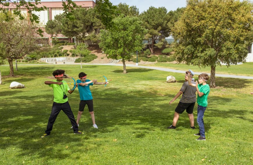 Kids engaged in an outdoor game using toy bows at a summer camp park.