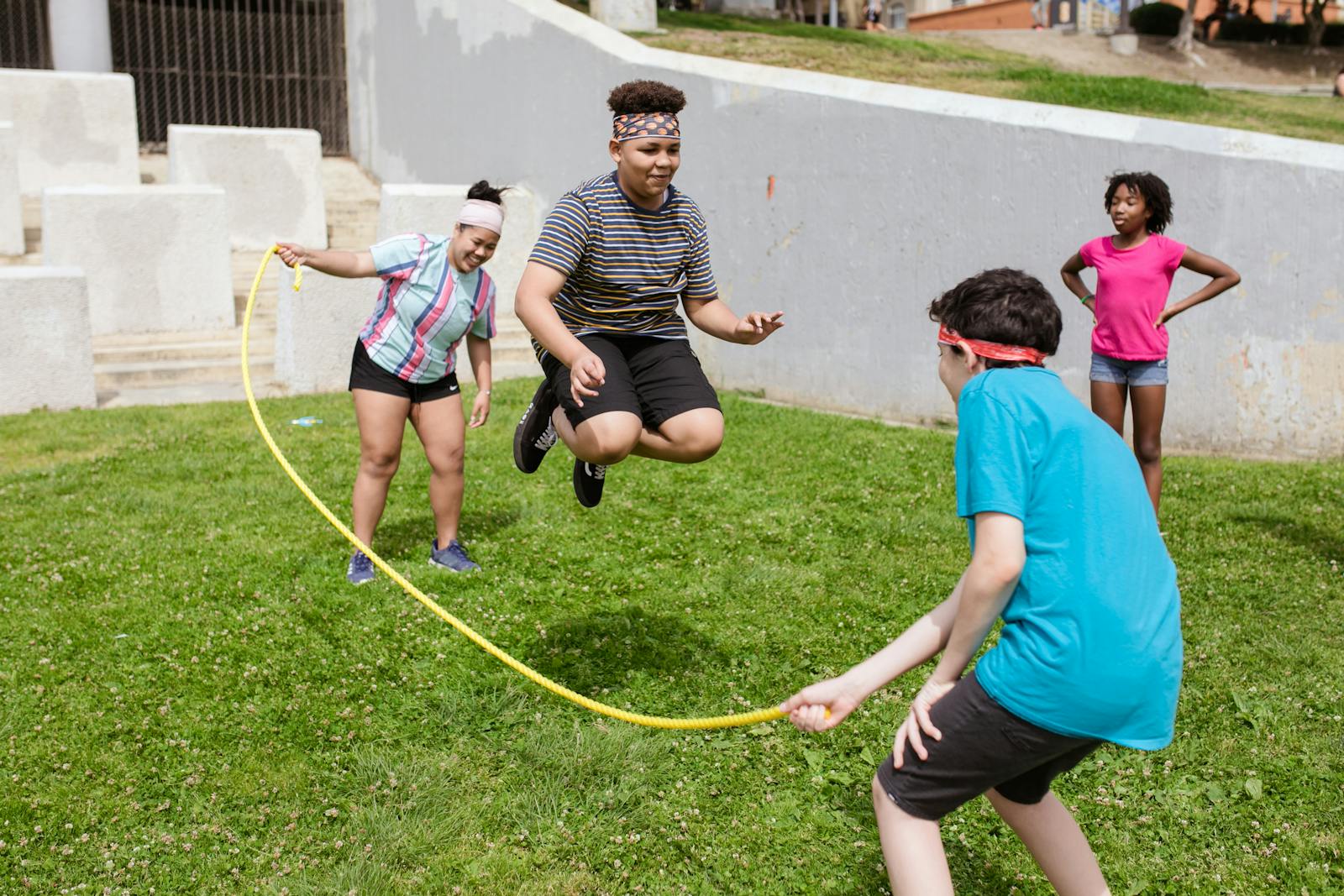 Group of diverse teenagers playing jump rope on a sunny day in a park, having fun and active outdoors.
