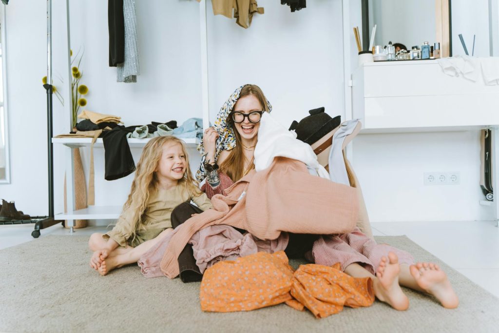 Happy mother and daughter laughing together while organizing clothes in a bright and cozy room.
