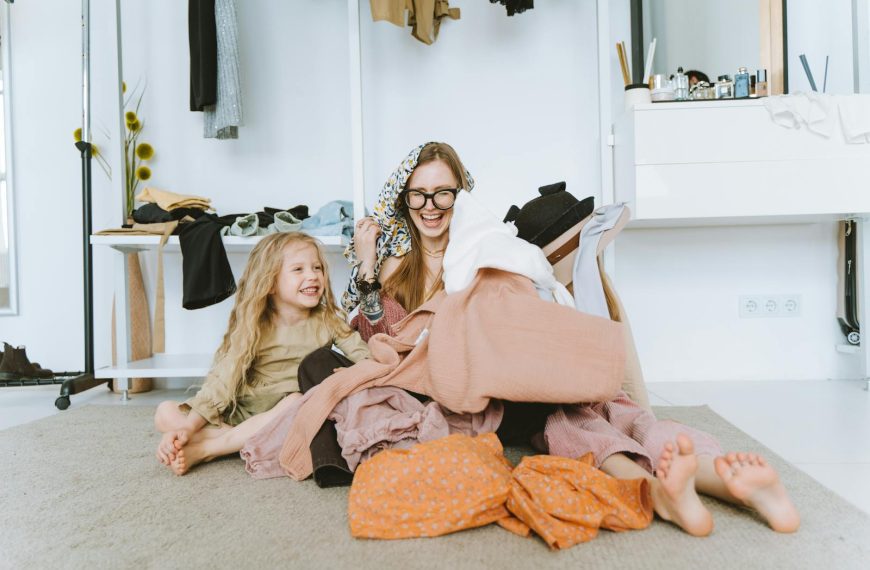 Happy mother and daughter laughing together while organizing clothes in a bright and cozy room.