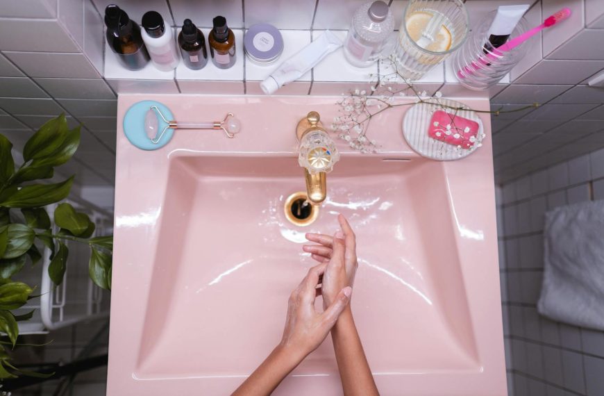 A stylish bathroom setup with skincare products and a person washing hands in a pink sink.