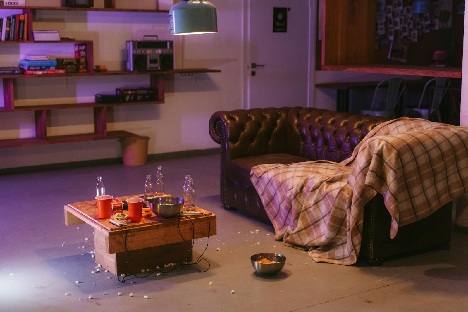 A cluttered living room with snacks, cola bottles, and a cozy sofa.