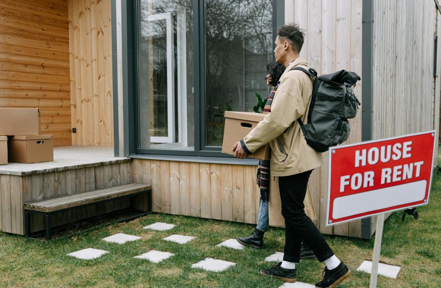 Young couple moving into a new rental home with boxes. Outdoor scene with a rental sign.