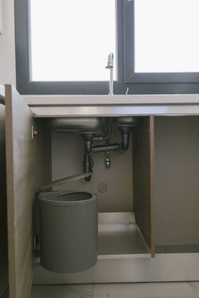 Under-sink view of modern plumbing with garbage bin in an Istanbul apartment kitchen.