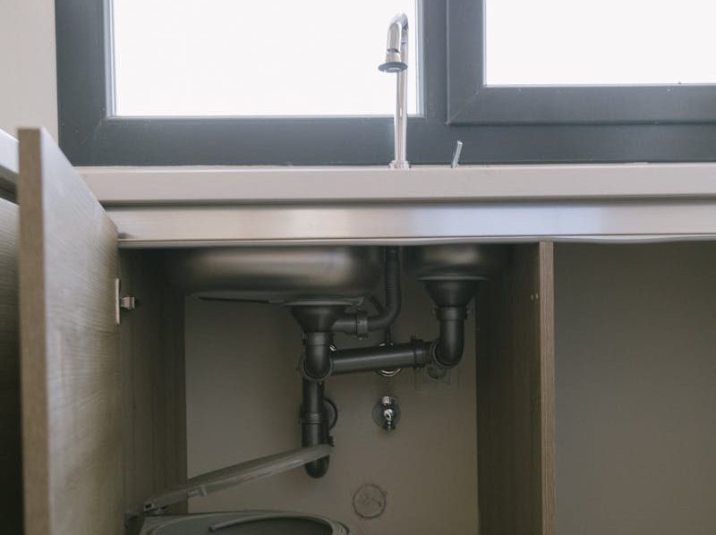 Under-sink view of modern plumbing with garbage bin in an Istanbul apartment kitchen.