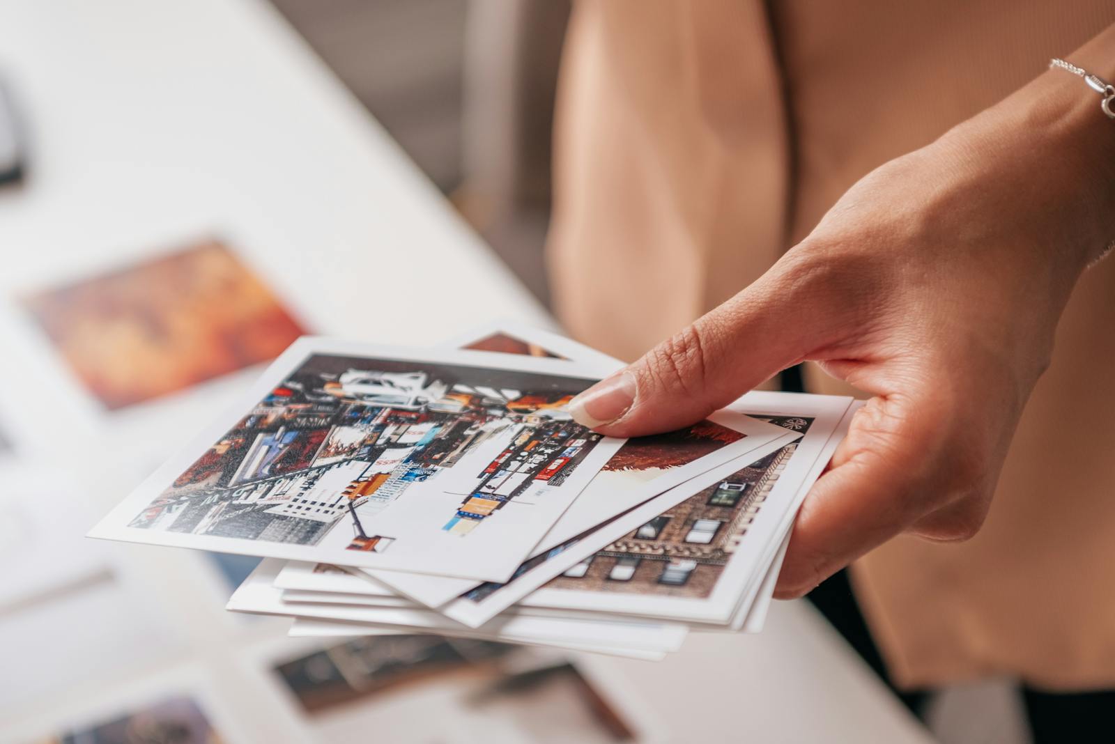 A hand holding printed photographs featuring urban cityscapes on a white table.