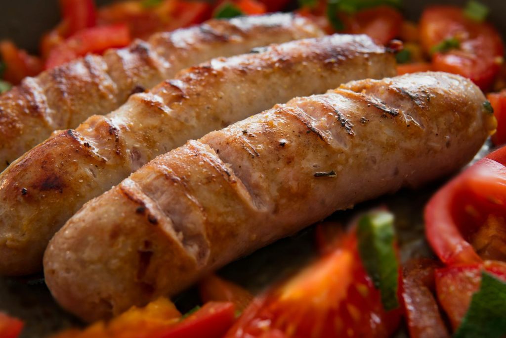 Close-up of juicy grilled sausages served with fresh sliced tomatoes.