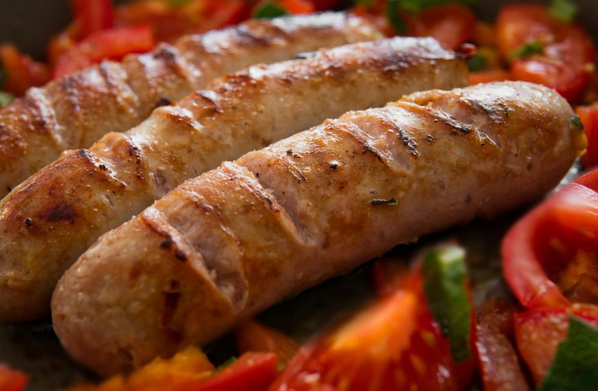 Close-up of juicy grilled sausages served with fresh sliced tomatoes.