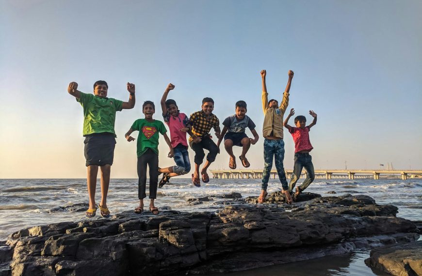 Group of kids joyfully jumping on rocks by the seaside. Fun and playful moment captured outdoors.