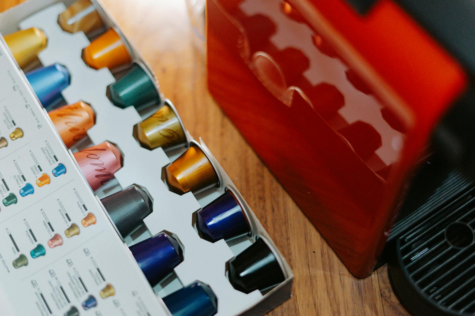 Close-up of colorful coffee capsules next to a coffee machine on a wooden table.