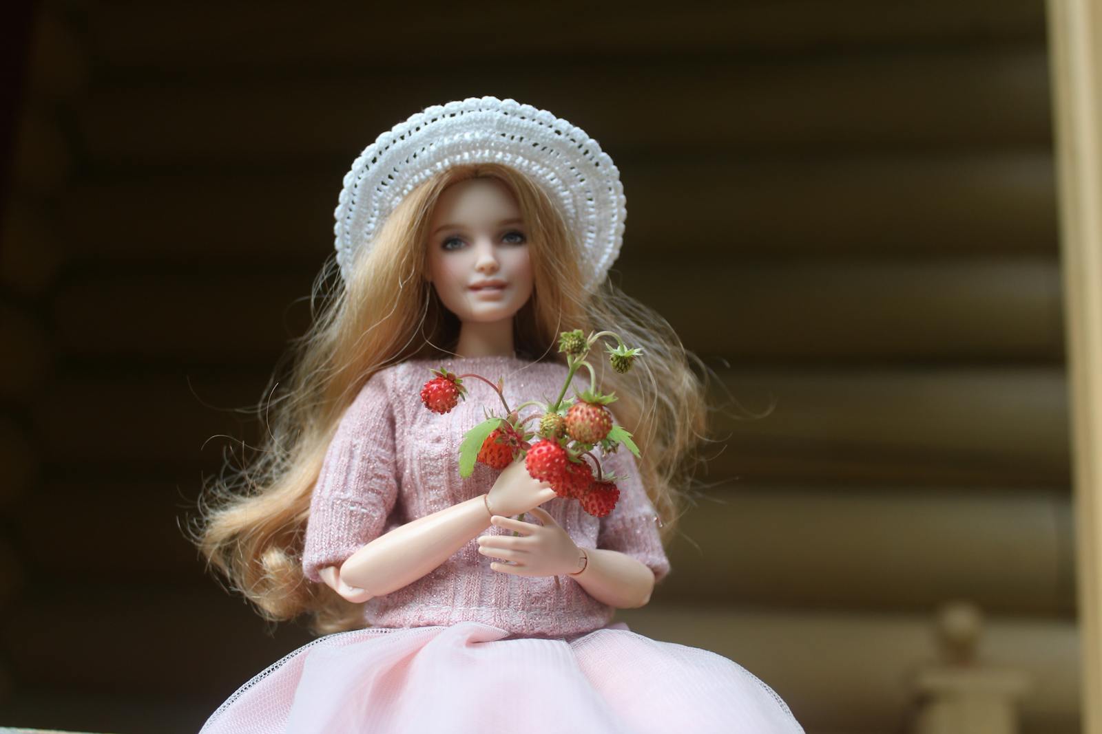 A beautiful doll wearing a pink dress and hat holds fresh strawberries, evoking a serene and elegant vibe.