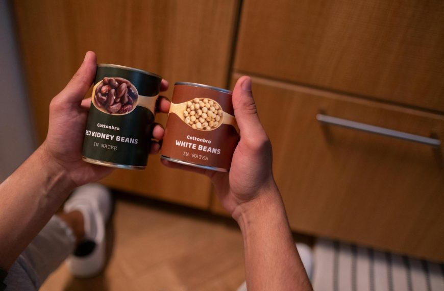 A person holding canned red kidney beans and white beans in a kitchen setting, emphasizing food storage.