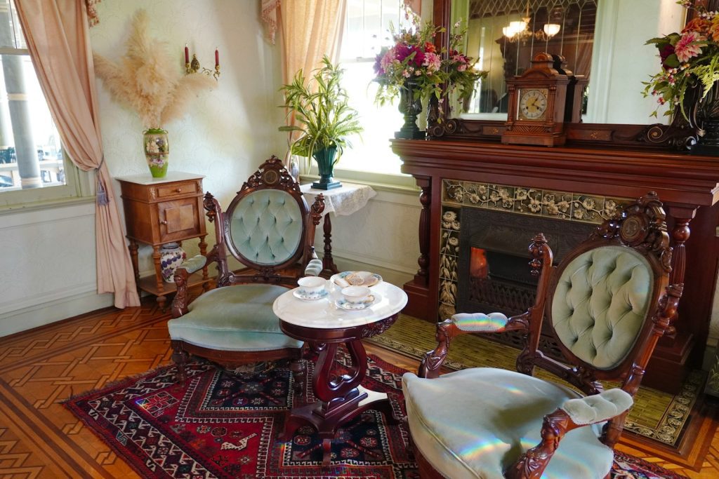 An antique parlor features chairs and a fireplace.