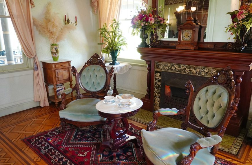 An antique parlor features chairs and a fireplace.