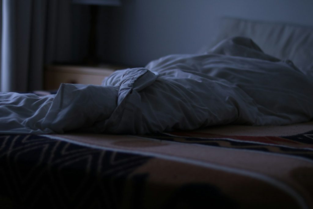 an unmade bed in a dark room with a window