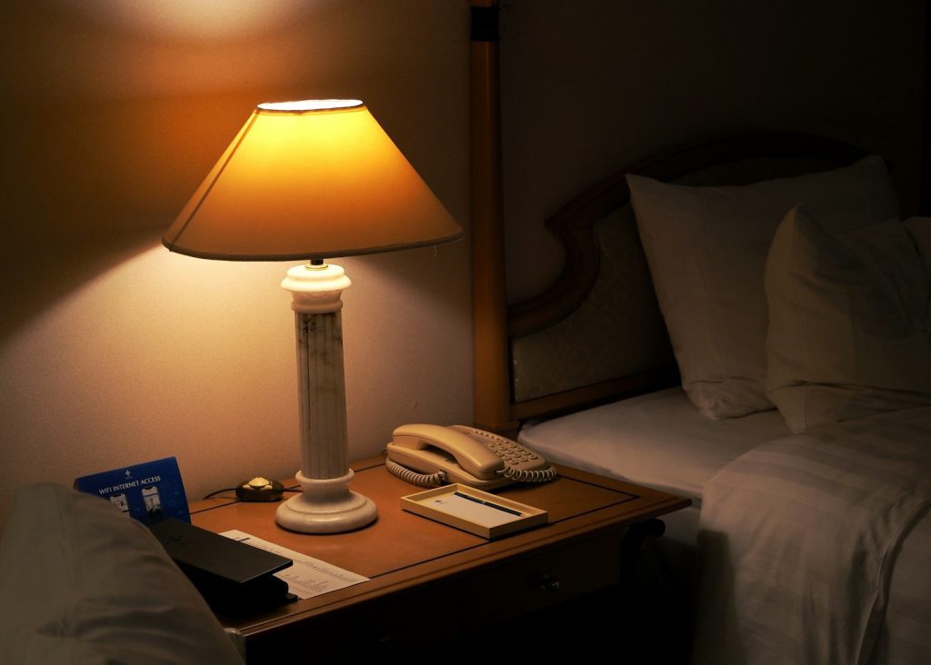 A lamp on a night stand next to a bed