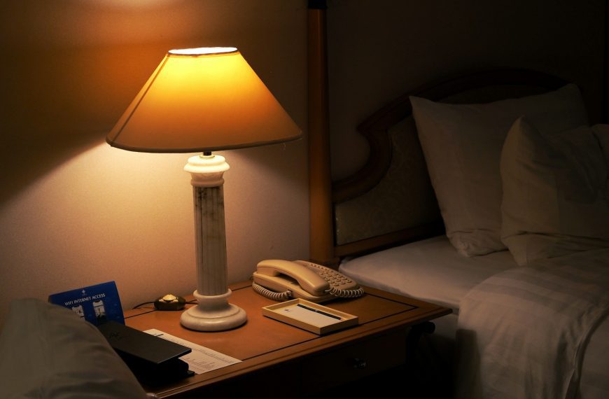 A lamp on a night stand next to a bed