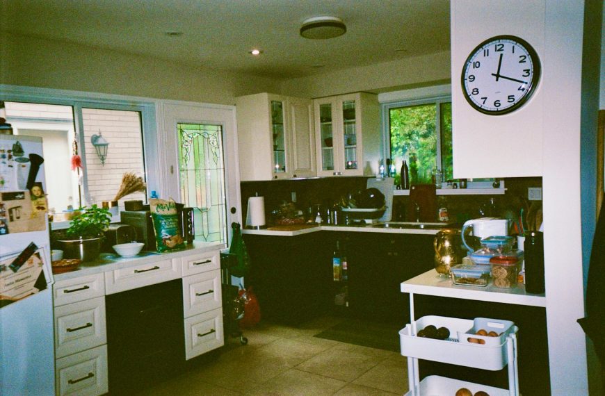 A kitchen is shown with a clock and cabinets.