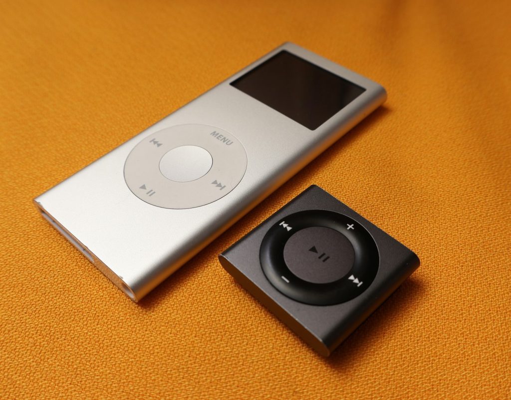 An iPod sitting next to an mp3 player on a bed