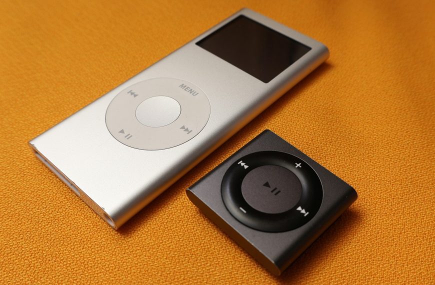 An iPod sitting next to an mp3 player on a bed